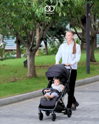 A mother pushing her child in a Koopers stroller through a serene park, emphasizing comfort and convenience for everyday outings in Malaysia.