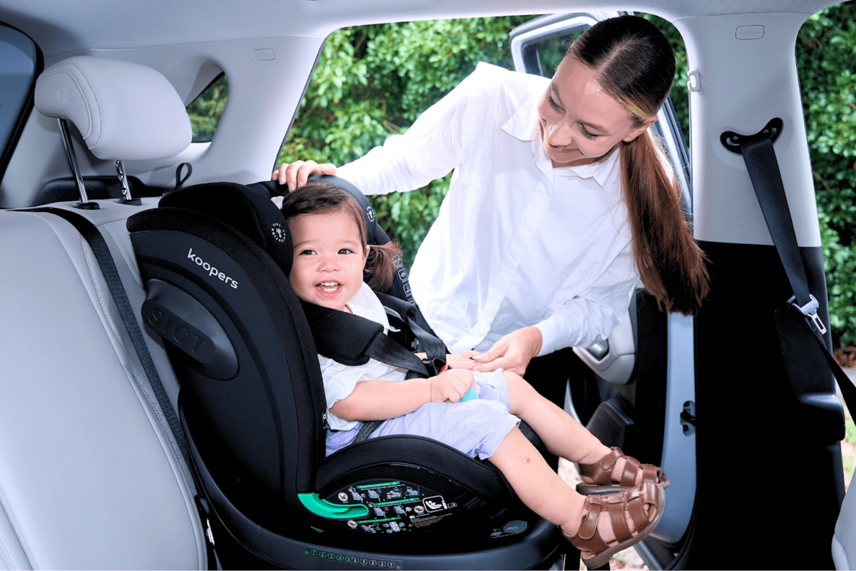 Parent securing a child in a Koopers Armour 360 car seat, emphasizing ease of use and advanced safety features.