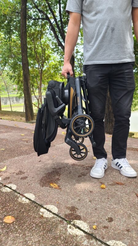 Man carrying the compactly folded Koopers Magic Rider 360 stroller, showcasing its lightweight and space-saving design.