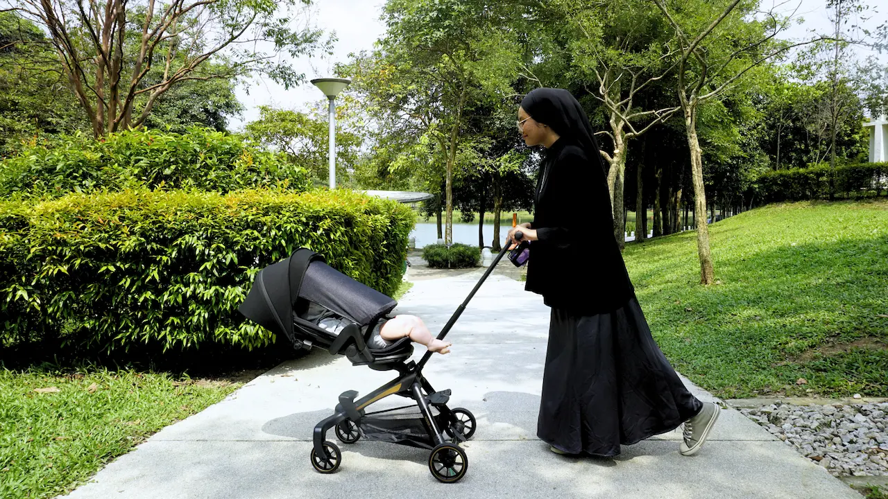 Mother pushing a Koopers Magic Rider 360 stroller with a baby, enjoying a serene walk in a park setting.