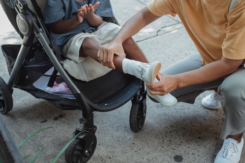 choosing-the-right-stroller-and-car-seat-for-your-newborn-8 Parent helping child near stroller during outdoor activity, highlighting everyday stroller usability and front-wheel stability.