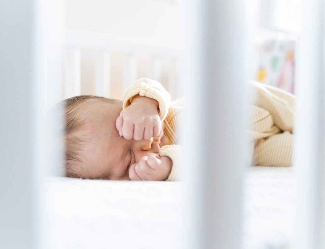 best-baby-sleep-tips-for-malaysian-parents-2 Baby rubbing eyes while lying in crib – showing natural sleep cues and early signs of tiredness in infants.