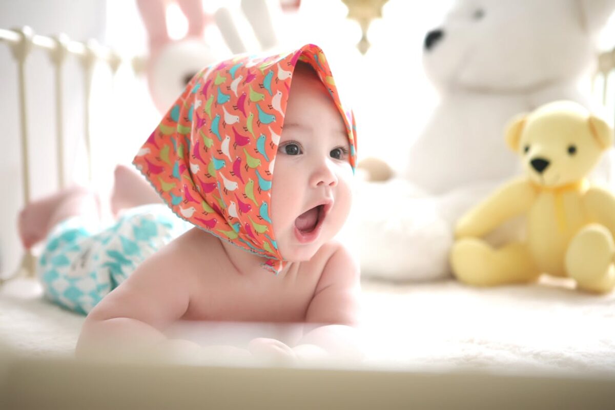 how-to-prepare-for-your-babys-first-year-1 Curious baby wearing a colourful bonnet, surrounded by toys – representing developmental play in early months.