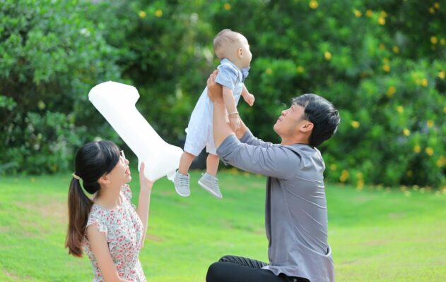How to Travel with a Baby in Malaysia Without the Stress 2 Happy parents lifting baby outdoors in a green park, enjoying family time and fresh air together