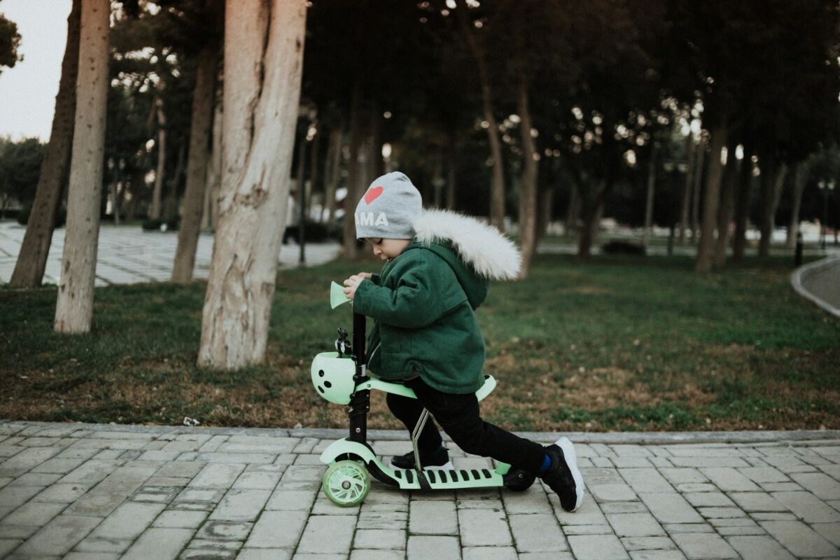 Malaysian toddler riding a Koopers baby scooter at the park, supporting balance and gross motor skill development