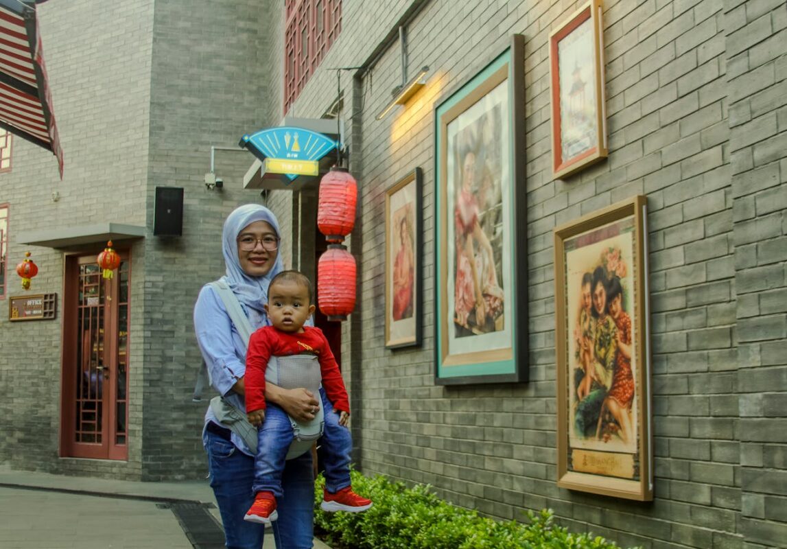 What to Pack in Your Baby’s Day-Out Bag in Malaysia 3 Malaysian mother wearing hijab carrying her baby in a front carrier outside a traditional Chinese-style building