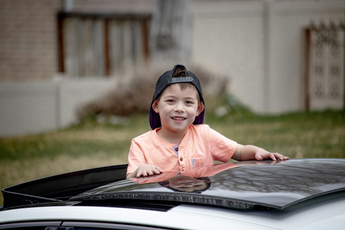 Young boy smiling while standing through a car sunroof without a booster seat — highlights the risks of improper child car safety in Malaysia.