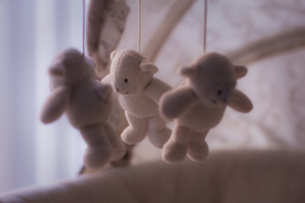 can-you-use-a-playpen-as-a-baby-cot-1 Soft plush teddy bear mobile hanging above a baby cot, symbolizing safe sleep environment considerations for Malaysian parents choosing between baby cots and playpens.