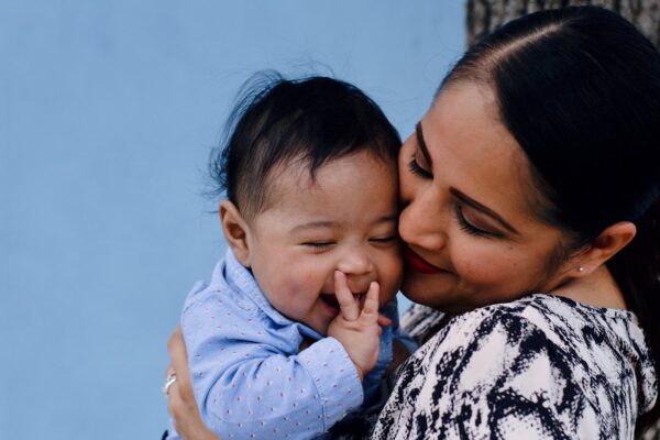 can-you-use-a-playpen-as-a-baby-cot-2 Smiling Malaysian mother cuddling her baby, reflecting parental care and decisions about safe sleep spaces like playpens versus baby cots.