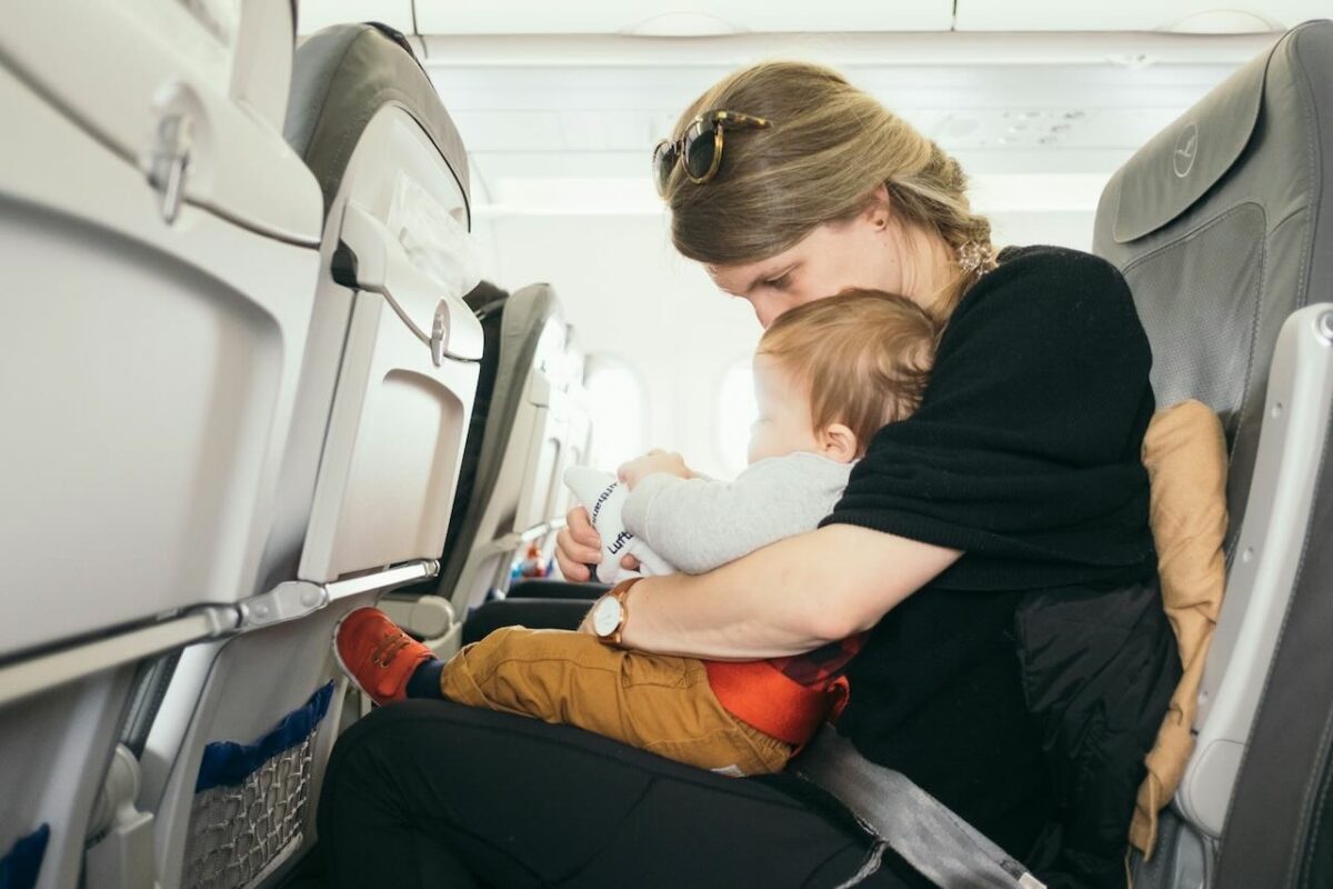 Mother flying with baby on lap in airplane seat, preparing for cabin stroller travel in Malaysia