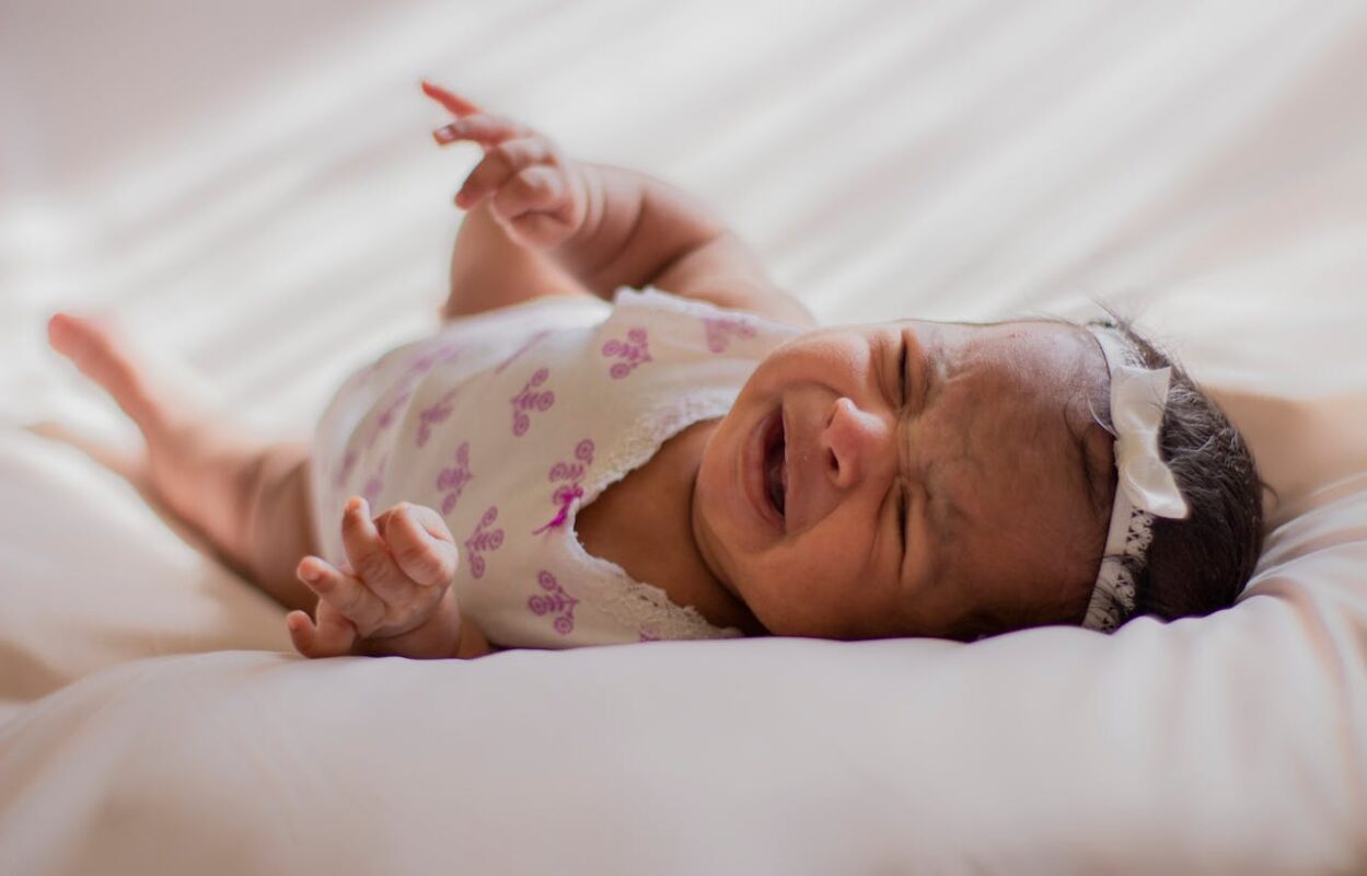Infant lying on bed crying, highlighting the struggles of colic and the potential benefits of gentle motion from electric baby swings in calming fussiness.