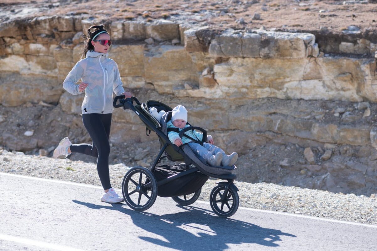 Active Malaysian mom jogging with baby in three-wheel jogger stroller on uneven outdoor terrain