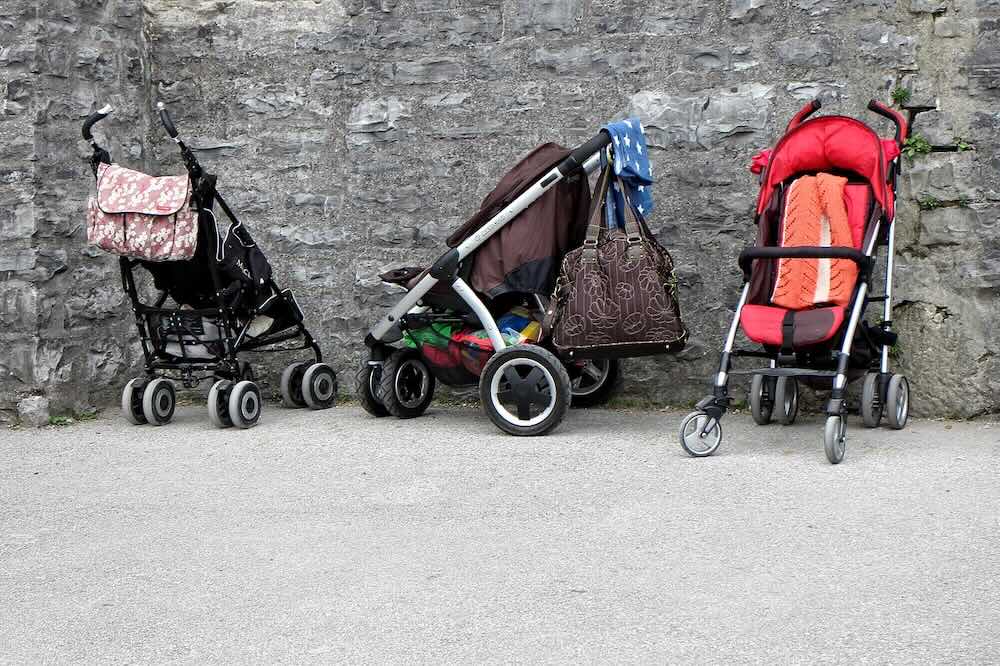 5 Travel-Friendly Baby Products You’ll Be Glad You Packed 16 Three baby strollers parked side by side on pavement against stone wall, showcasing different stroller styles for parents in Malaysia