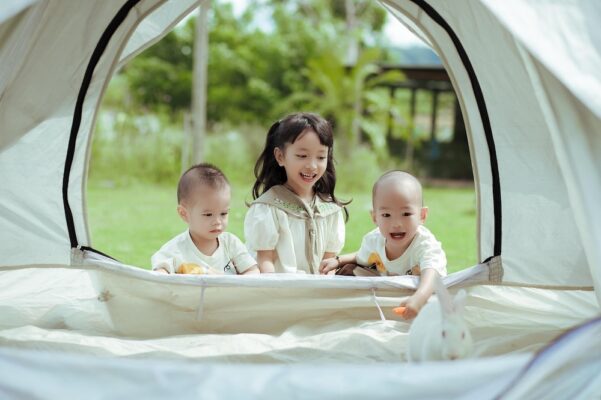 baby-car-seats-in-malaysia-7 Three smiling Asian children playing inside a white camping tent outdoors, enjoying family time and nature