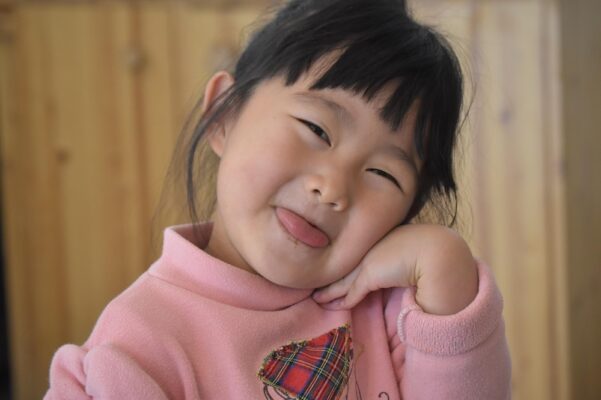 baby-car-seats-in-malaysia-8 Asian toddler girl wearing a pink sweater making a cute face and sticking out her tongue while posing indoors