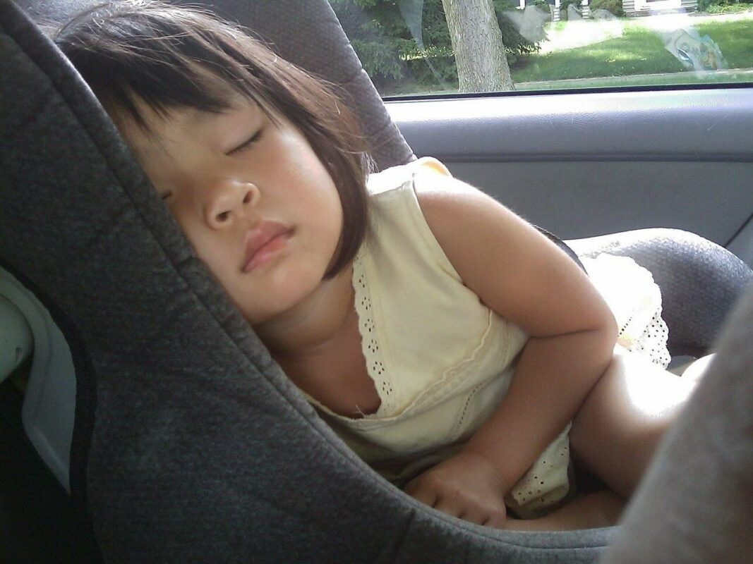 Young Asian girl peacefully sleeping in a grey car seat inside a vehicle, showing comfort and safety during travel