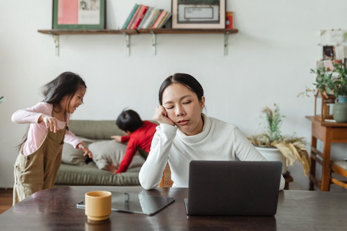 Malaysian mother comparing baby gear online while her children play in the background — balancing parenting and smart shopping decisions.