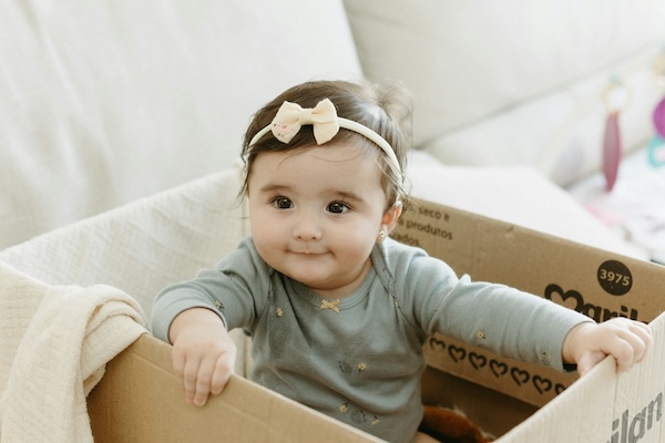essential-daycare-car-seat-and-stroller-tips-5 Smiling baby girl in a cardboard box at home, symbolising the daily hustle of getting ready for daycare.