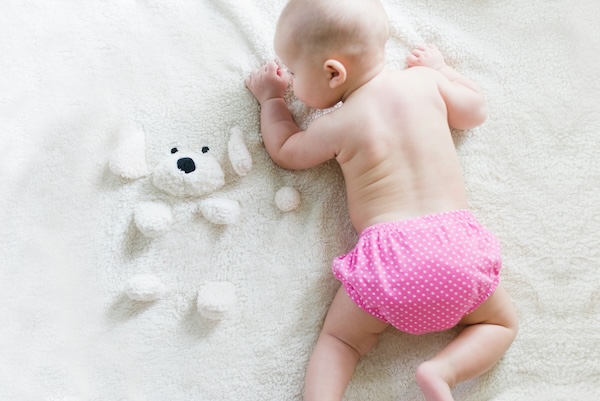 essential-daycare-car-seat-and-stroller-tips-7 Baby in pink polka dot diaper crawling on soft white blanket, representing morning routines before daycare.