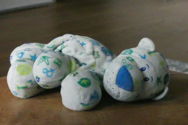 essential-travel-gear-for-parents-flying-with-a-baby-1 ALT text: Soft white stuffed animal with blue and green patterns lying on a wooden surface in a dimly lit room.