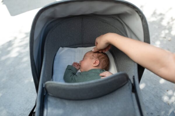 how-to-fold-store-maintain-koopers-stroller-7 Sleeping baby in a grey stroller bassinet being gently soothed, highlighting the importance of comfort and maintenance.