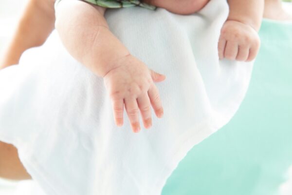 how-to-travel-light-as-a-malaysian-parent-without-sacrificing-baby-comfort-6 Close-up of a baby’s hand resting on a white cloth, on a person's shoulder.