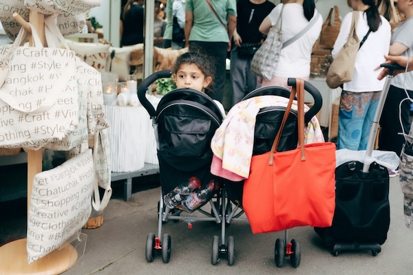 how-to-use-baby-stroller-in-theme-parks-malls-public-transit-without-hassle-5 Child seated in a twin stroller at a busy shopping market, demonstrating practical stroller use for Malaysian malls and retail spaces