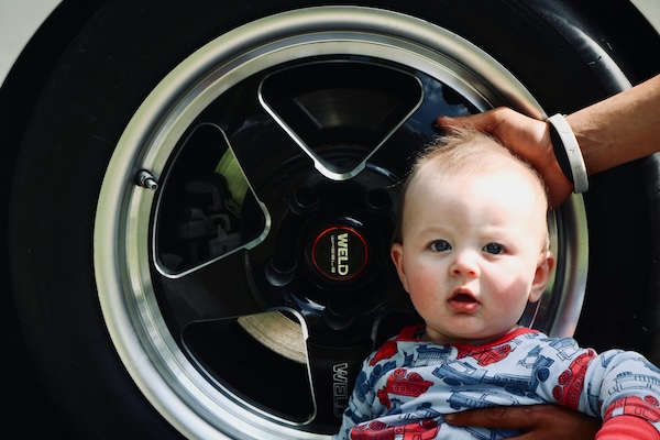 is-your-baby-car-seat-still-safe-after-a-minor car accident-5 Baby sitting beside a car tyre – highlighting importance of checking child car seat safety after a crash