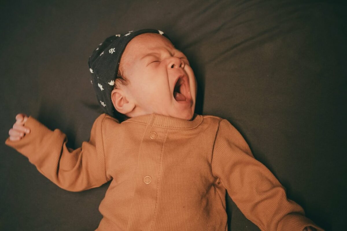 Yawning baby wearing hat – represents tiredness and stress after minor accident, reminder to assess baby car seat condition