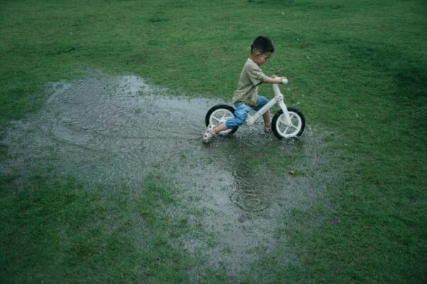 ride-on-toys-for-kids-are-they-safe-for-urban-environments-4 Young boy riding a white balance bike through a puddle on grassy field, highlighting active outdoor play with ride-on toys.