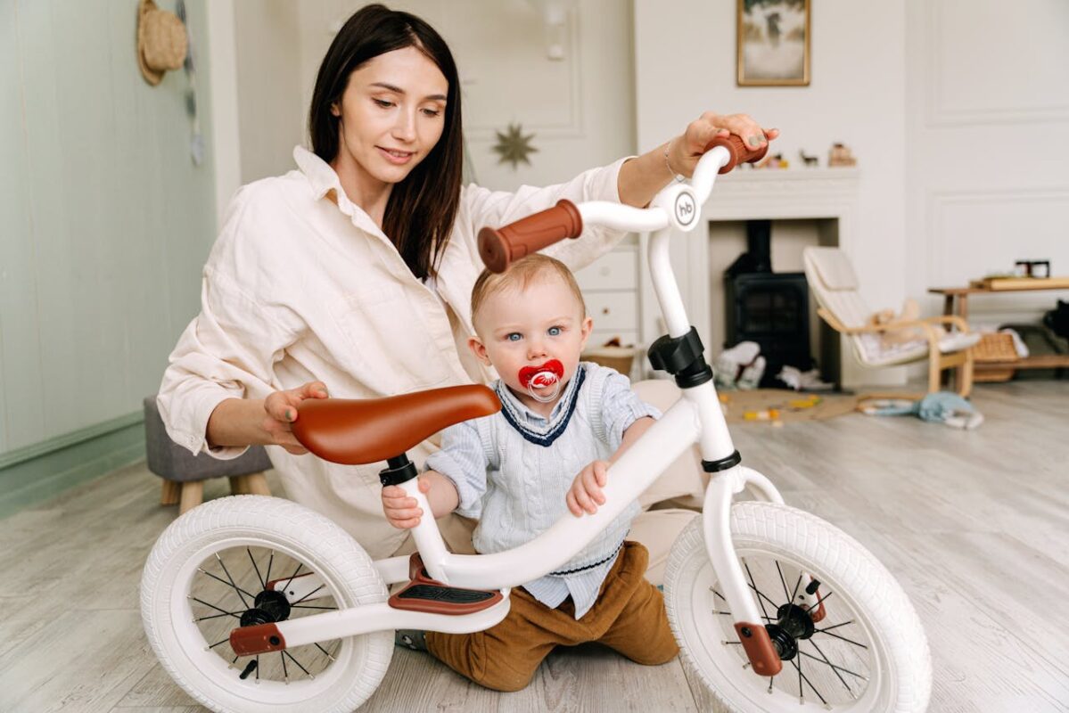 Mother helping toddler with a white balance bike indoors, demonstrating safe urban play options with ride-on toys for Malaysian families.