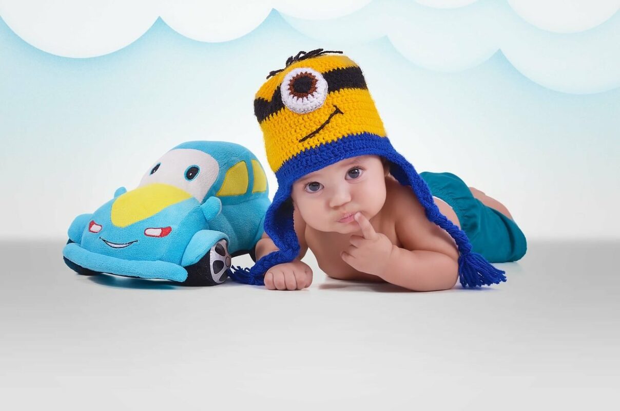 Cute baby in colorful hat with toy car symbolizing early love for cars and car safety gear