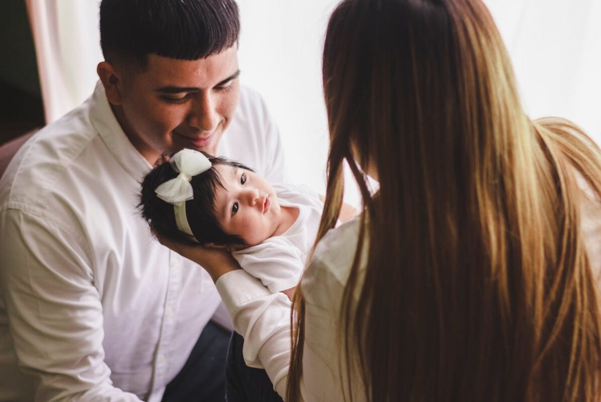 Father holding baby girl in his arms while mother looks on, emphasizing the importance of baby comfort and gear fit.