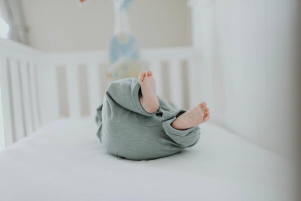 baby-cot-bed-care-malaysia-1 Baby lying comfortably in cot with legs raised, representing baby comfort and safe sleep in Malaysia