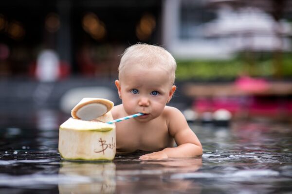 how-to-keep-baby-cool-in-stroller-malaysia-2 Baby staying hydrated by drinking coconut water, symbolizing keeping cool under Malaysia’s tropical sun