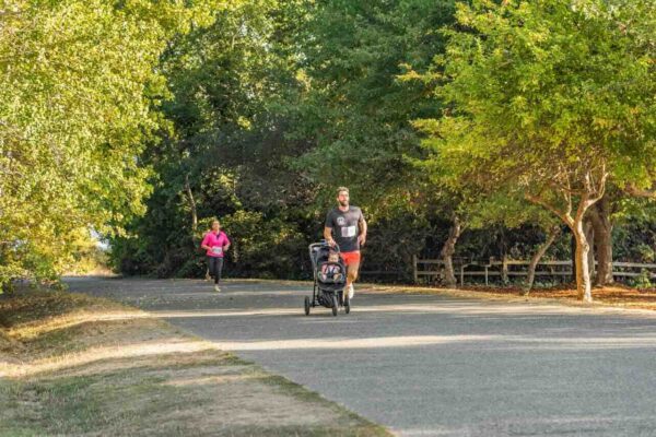 jogger-stroller-run-with-baby-safety-malaysia-2 Parent jogging with a baby in a jogger stroller on a shaded park path in Malaysia, demonstrating safe stroller running practices.