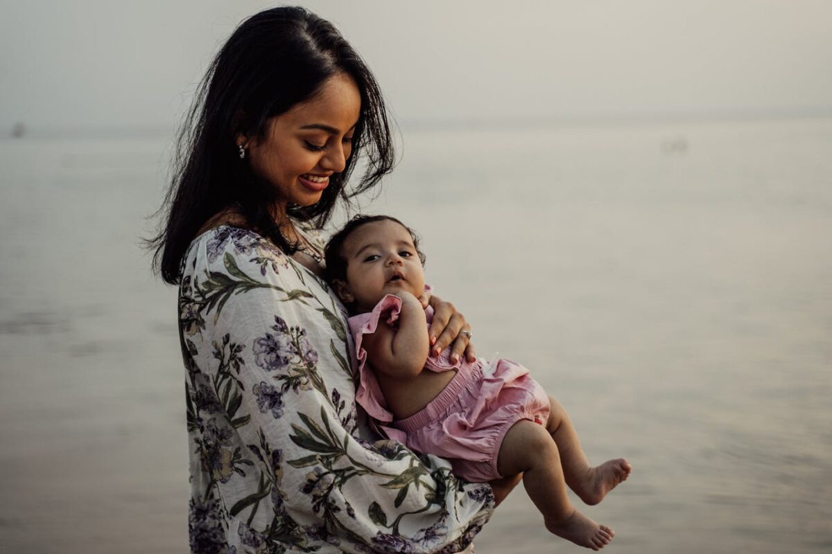 travel-cot-maintenance-tips-malaysian-parents-4 Mother holding her baby by the beach during a relaxing family getaway.