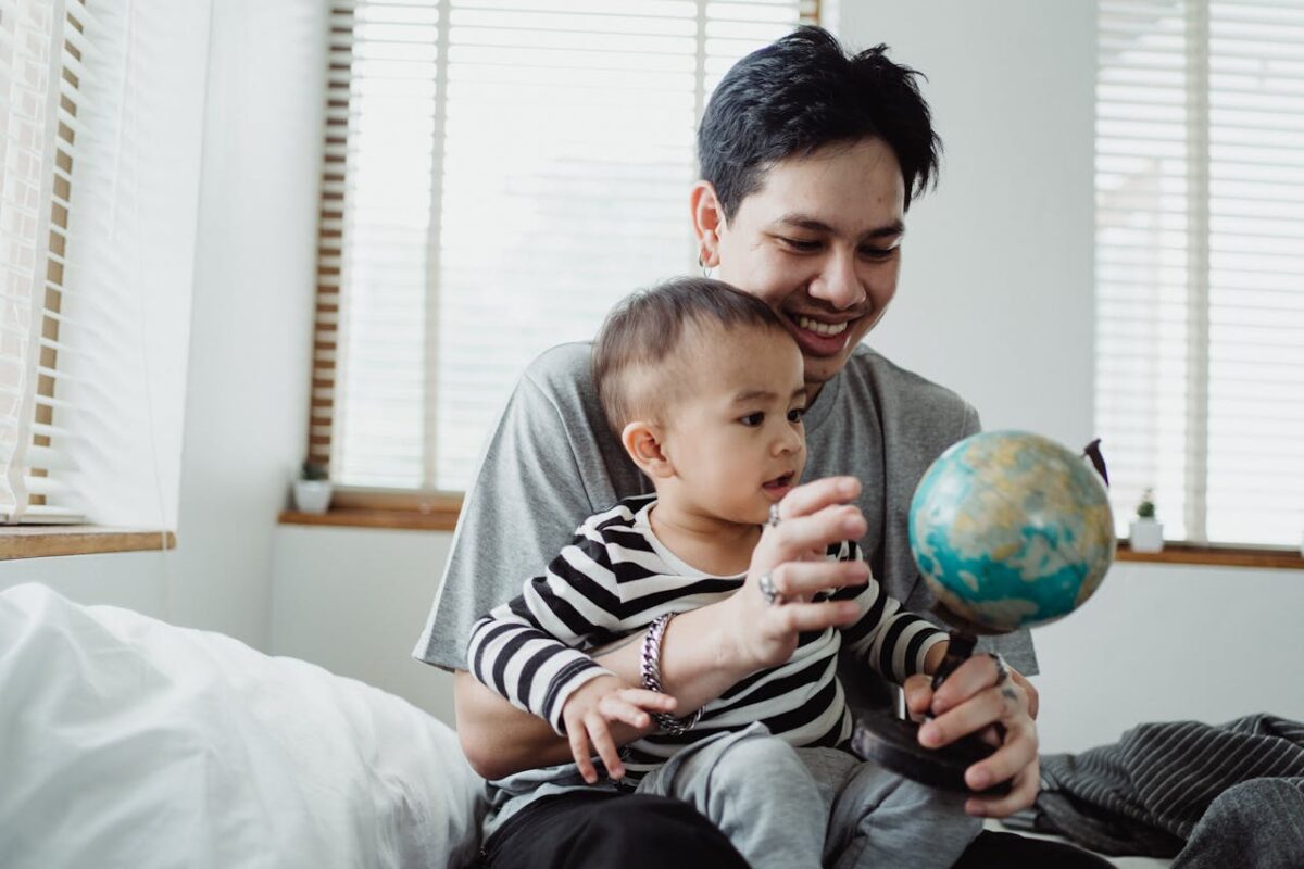 Father teaching his baby about travel using a globe while preparing for a family trip.