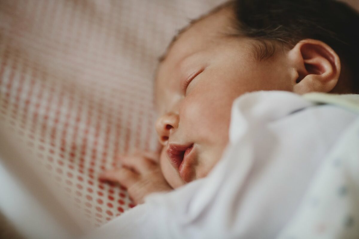 Beautiful newborn child lies on a bed and sleeps Newborn sleeping peacefully, showing the snug and secure sleep needed during the early baby cot stage.