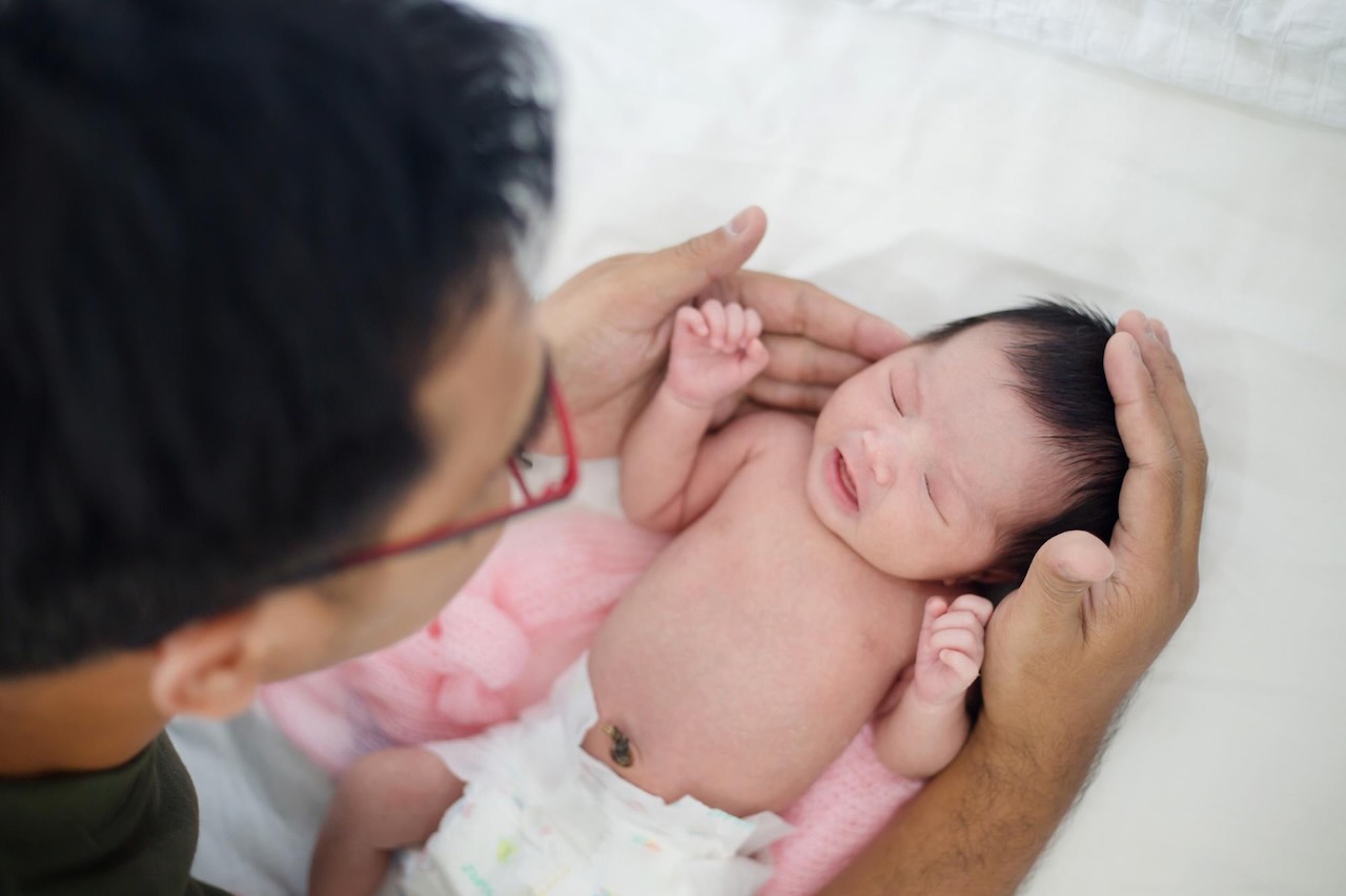 new-parents-tips-for-new-mums-dads-5 Father gently holds his newborn’s head and body during a careful health check.
