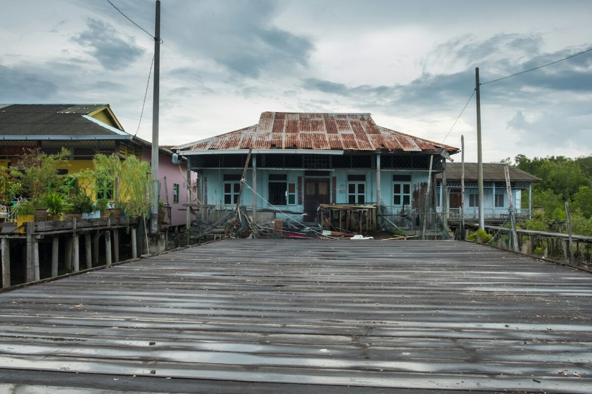 balik-kampung-with-baby-tips-for–parents-13 Traditional Malaysian kampung houses on stilts over water with wooden bridge for balik kampung Raya, colorful rustic village scene highlighting uneven paths needing travel cots and strollers Malaysia.