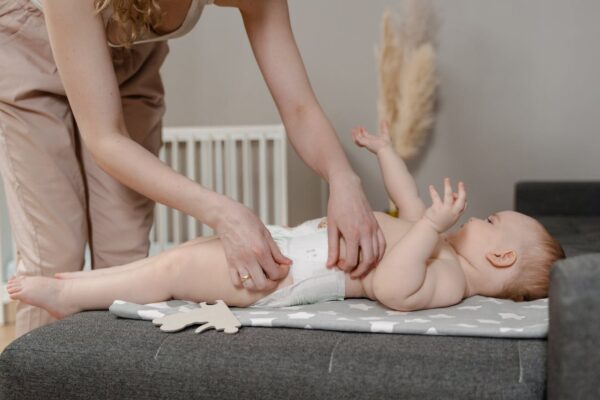 building-strong-bonds-with-your-newborn-daily-11 Malaysian mum changing diaper of happy newborn baby on mat, daily bonding routine with Koopers playpen baby cot nearby for safe play.