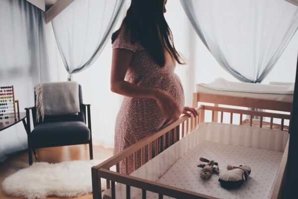 parents-guide-how-to-design-and-set-up-a-baby-nursery-1 Expectant parent preparing a baby nursery with a baby cot, soft bedding, and natural light before baby arrives.